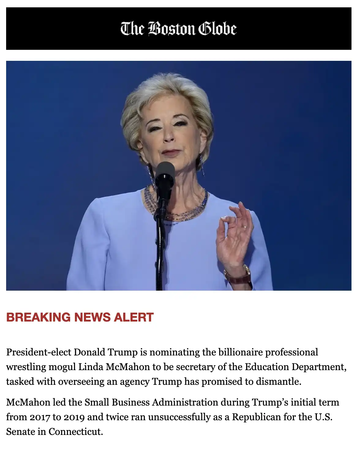 The image shows a woman with short blonde hair speaking into a microphone, wearing a light blue top and jewelry, against a…