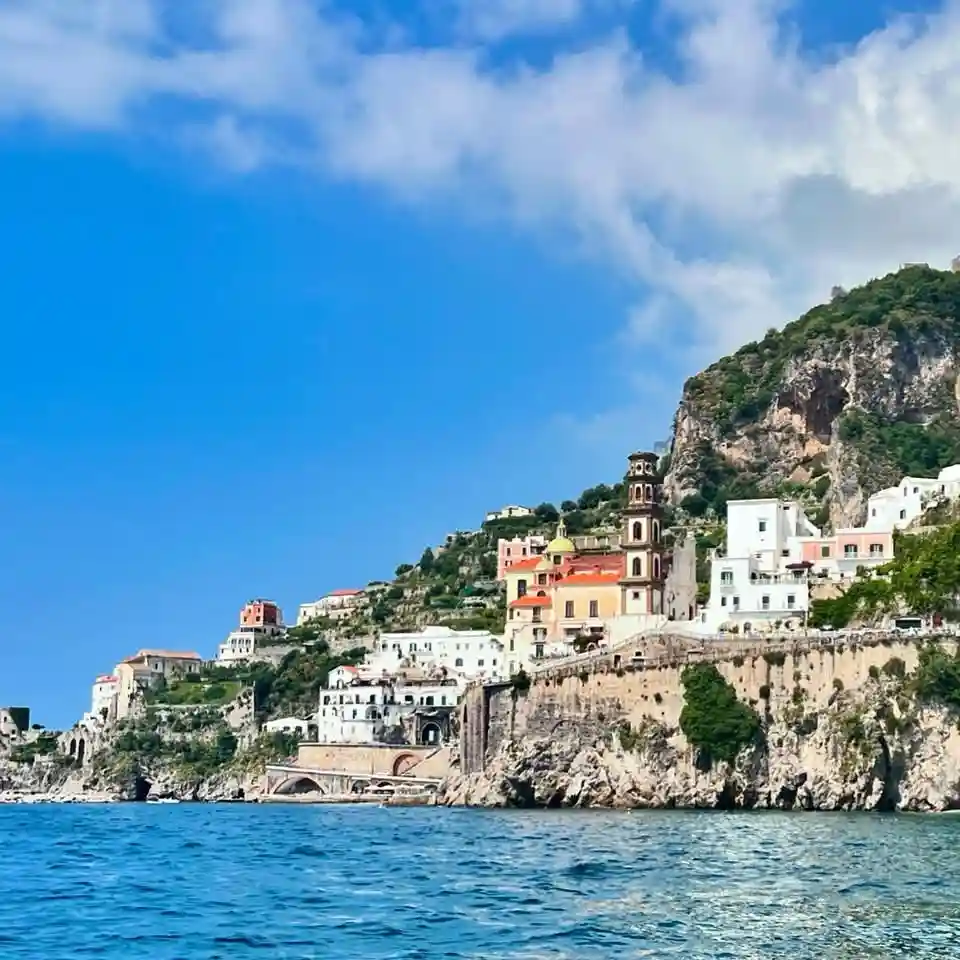 A scenic photo of a coastal town with colorful buildings clinging to a rocky cliffside under a bright blue sky with…