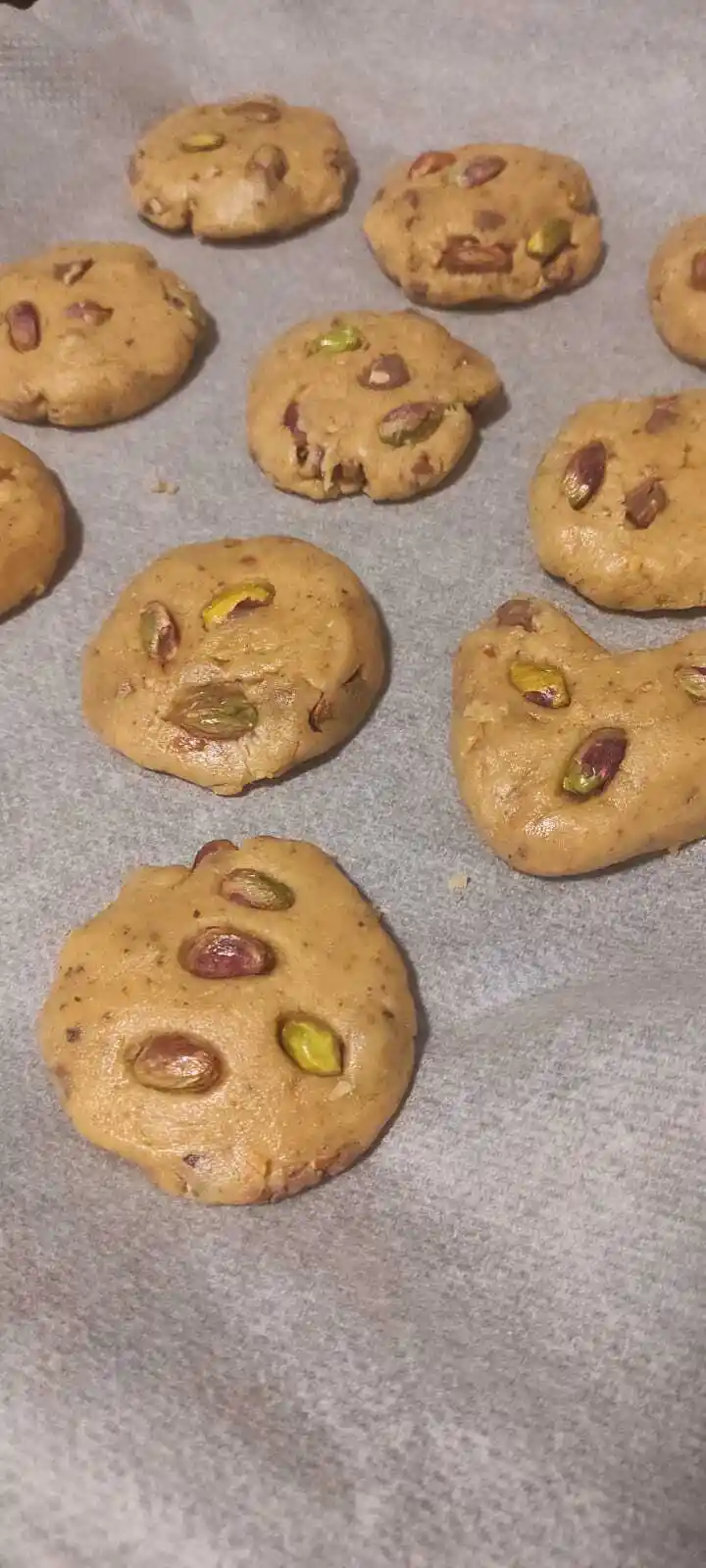 Several unbaked, round, golden-brown cookie dough balls with visible green and brown pistachios embedded in them are…