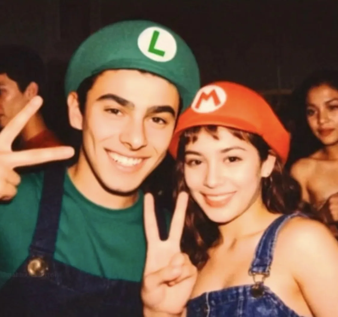 A young man and woman pose together at a party, both dressed as Mario and Luigi from the Super Mario video game series. The…