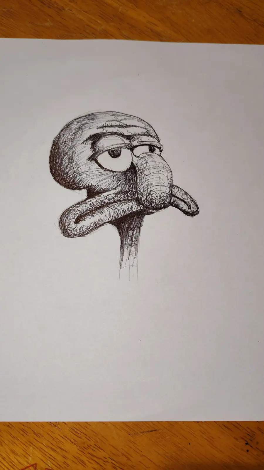 A hand-drawn pencil sketch on white paper shows a cartoonish, exaggerated squid-like face with large eyes, a bulbous nose…
