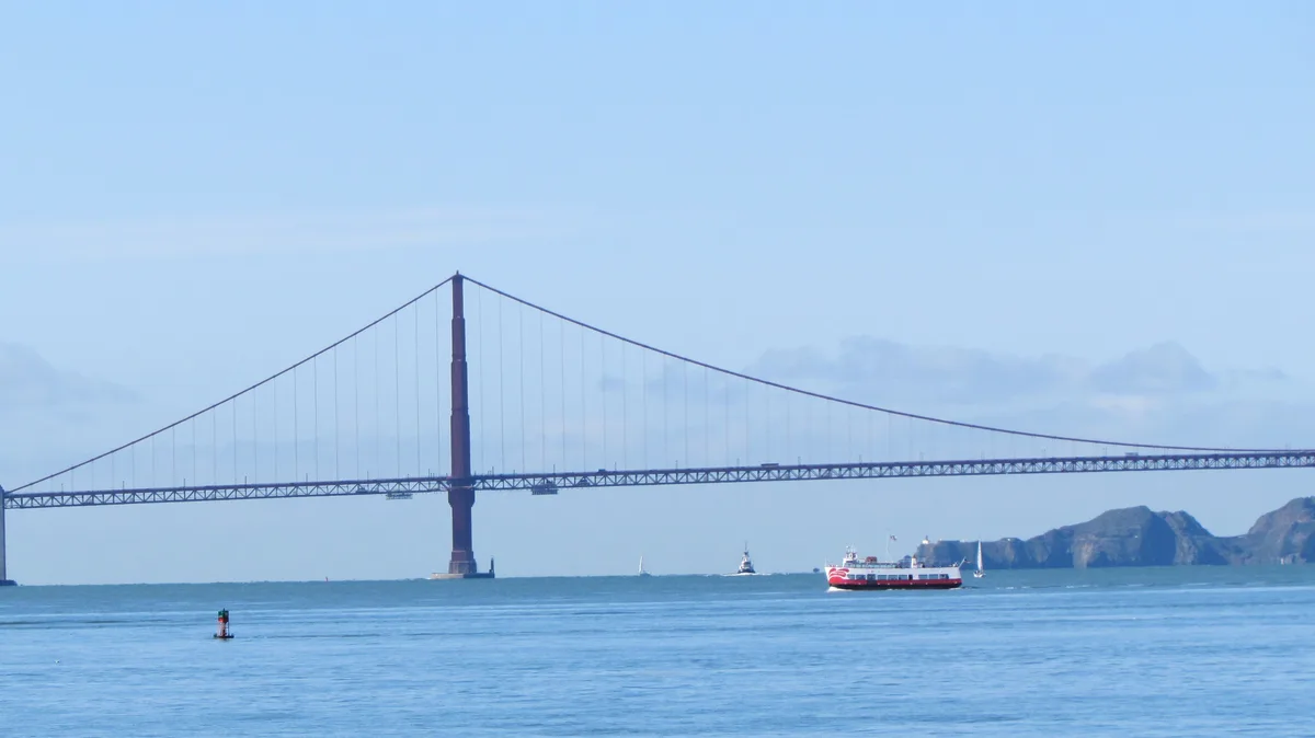 A scenic photo of the Golden Gate Bridge in San Francisco under a clear blue sky, with several boats on the water in the…