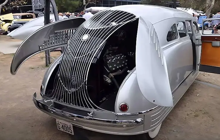 a silver vintage car with its front hood and side doors open, revealing an interior with a bar and seating. the car has a…