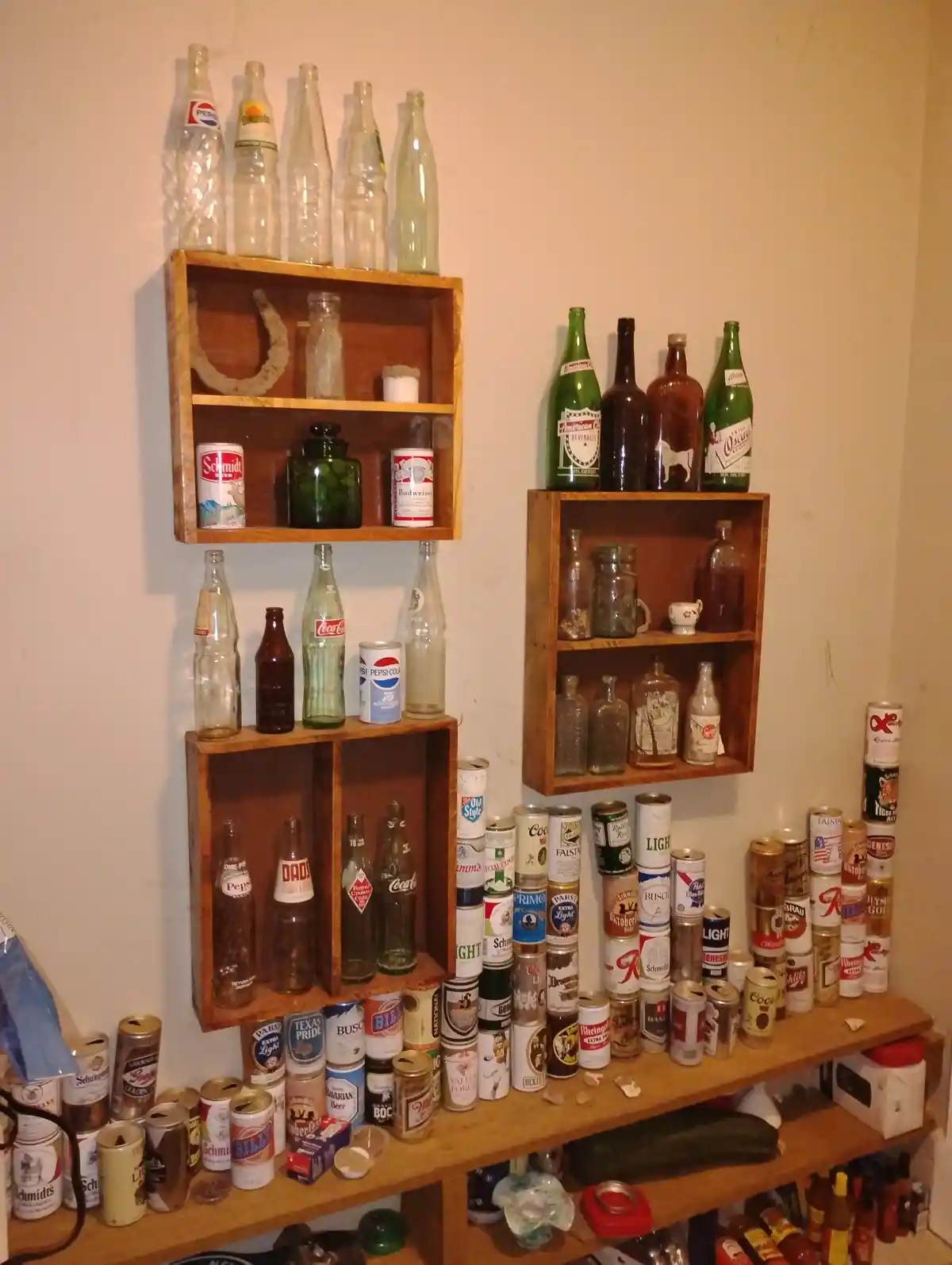 A wall-mounted wooden shelving unit displays numerous vintage glass bottles and aluminum beverage cans, including…
