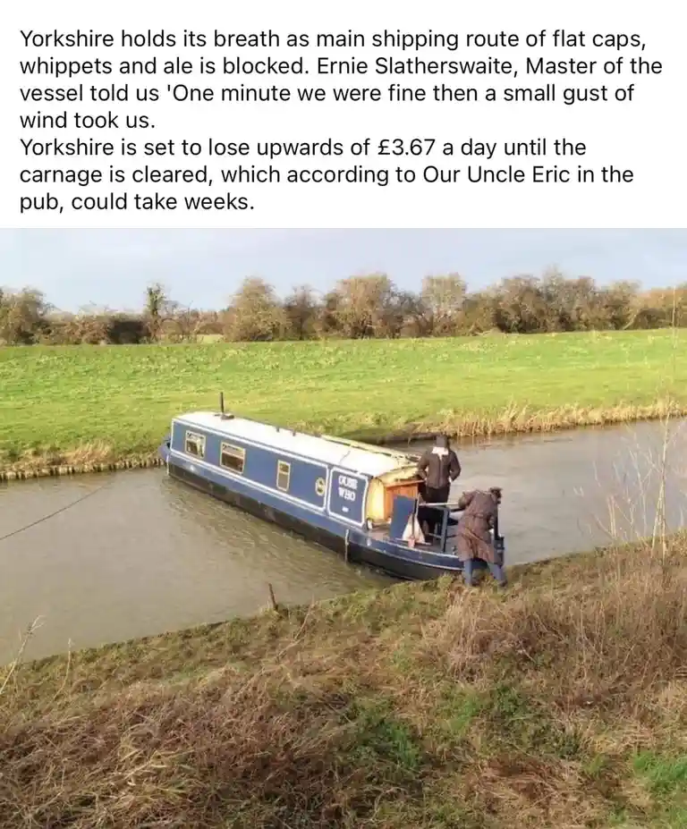 A blue and white narrowboat is stuck sideways on a canal bank, with two men in coats trying to pull it free. The background…