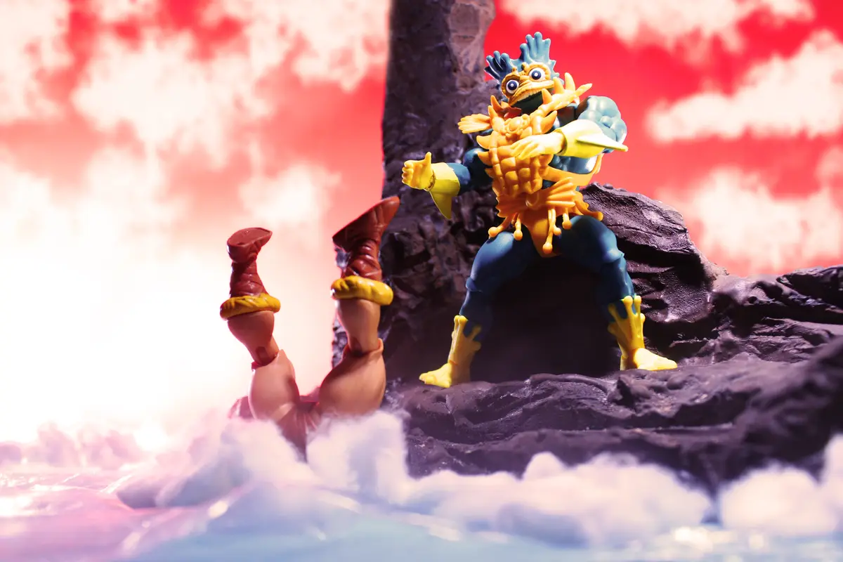A toy figure of the My Hero Academia character All For One stands triumphantly on a rocky outcrop against a red sky, while…