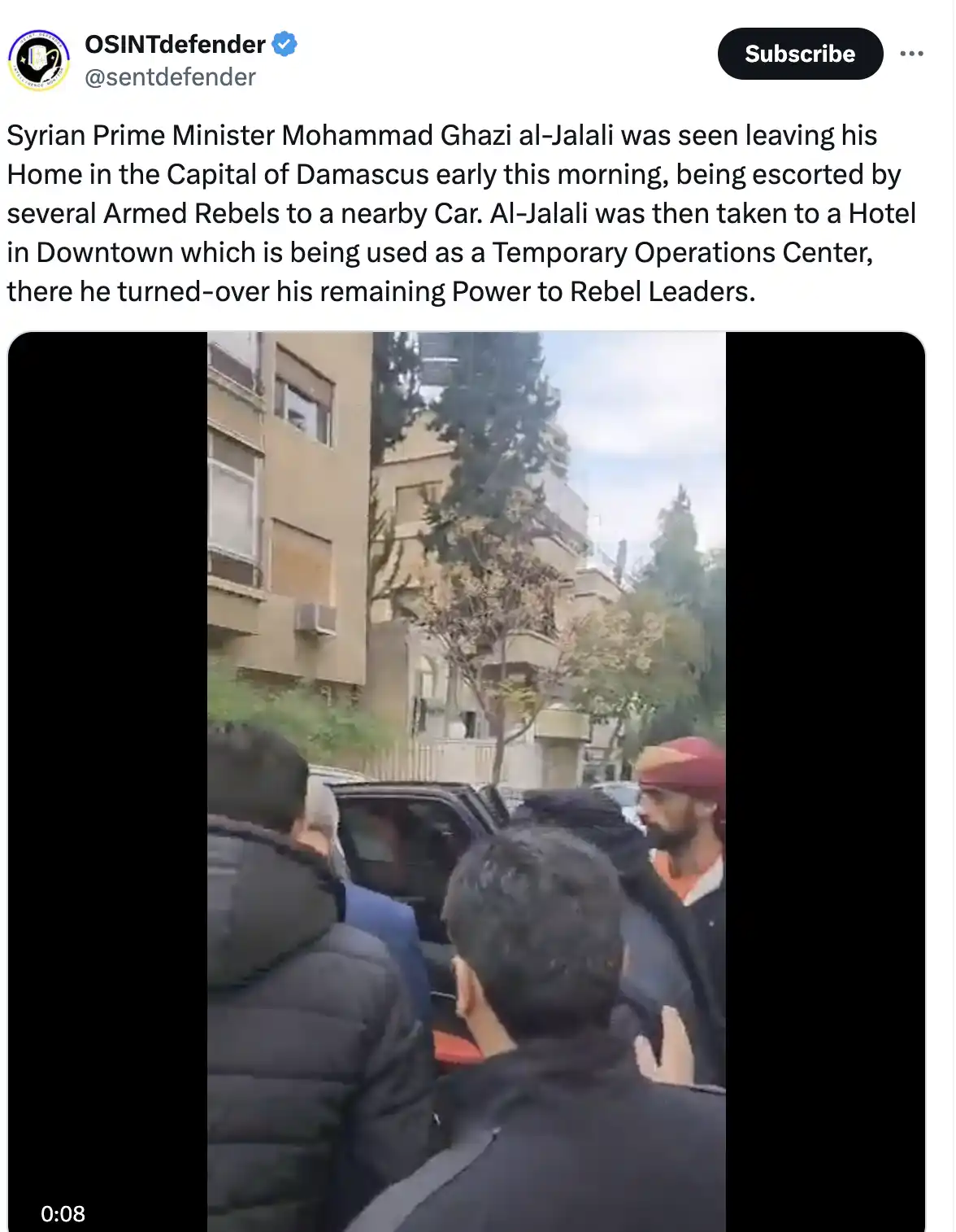 A screenshot of a social media post showing a video clip where a man in a suit is being escorted by armed men toward a car…