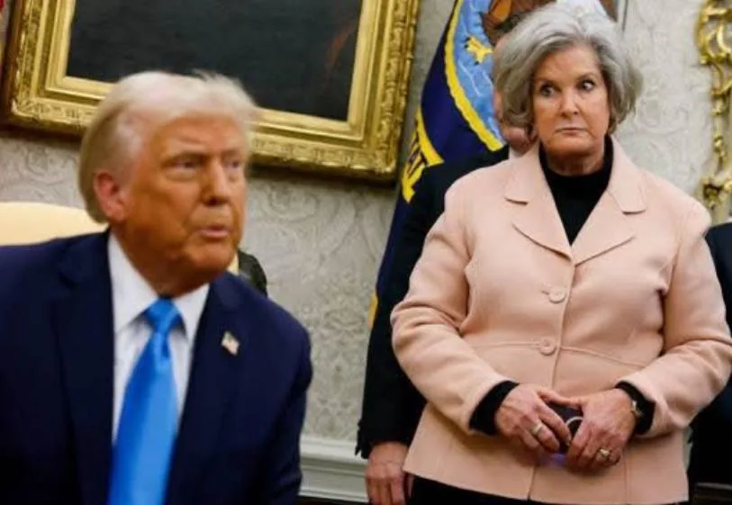 A photo shows Donald Trump seated in a formal room, looking slightly to his right with a serious expression, while a woman…