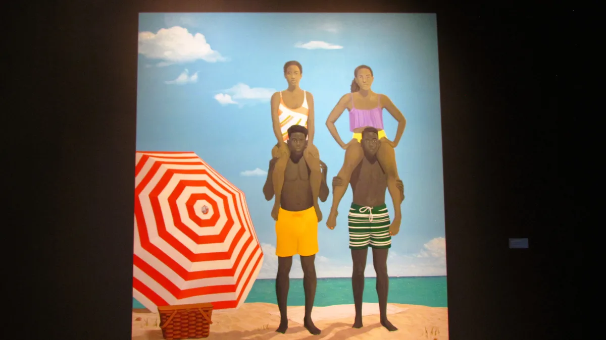 A photograph of a painting showing two Black men in swim trunks standing on a beach, each carrying a Black woman on their…