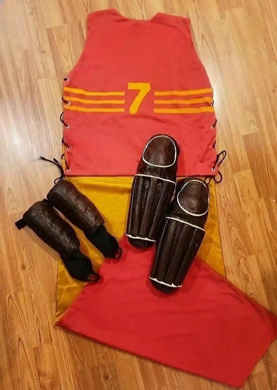 A red and yellow sports jersey with the number 7 is laid out on a wooden floor, accompanied by four brown leather-like…