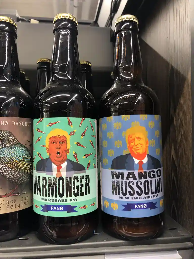 Two dark beer bottles sit side-by-side on a shelf, both featuring stylized portraits of Donald Trump. The left bottle has a…