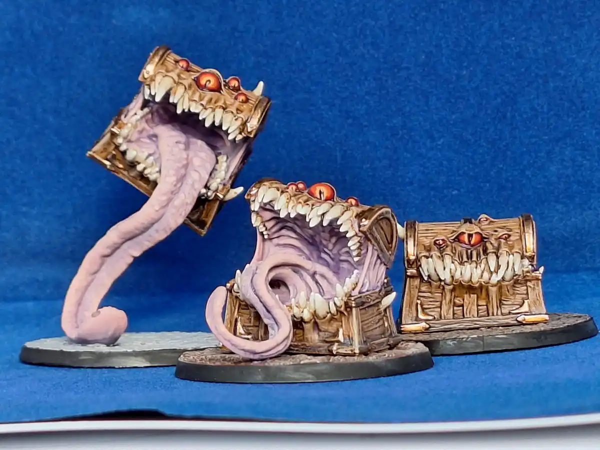Three intricately painted miniature treasure chests, each with a monstrous face featuring sharp teeth, glowing red eyes, and…