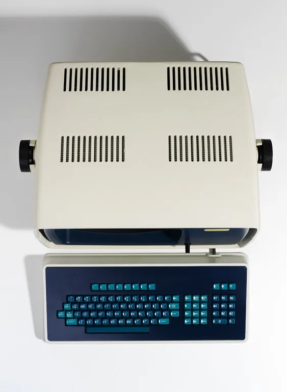 A vintage beige and blue portable computer with a split keyboard design is shown from above against a white background. The…