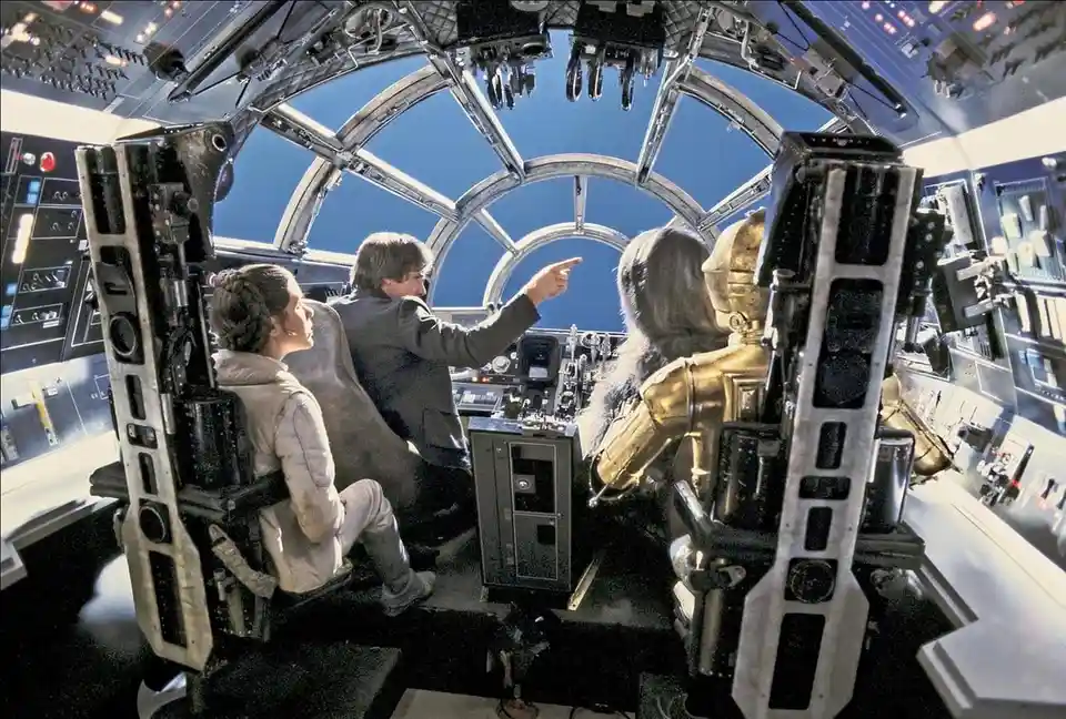 Inside the Millennium Falcon's cockpit, Han Solo points out the window while Leia Organa and Chewbacca look on. The overlaid…