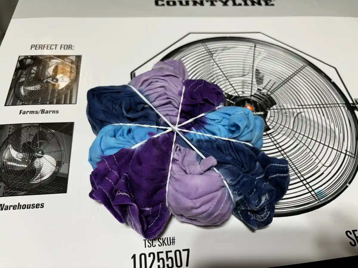 A tie-dyed shirt, bound in a star pattern with white string, is placed on top of a product box for a Countyline industrial…
