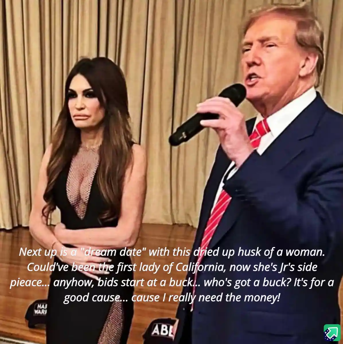 A man in a suit holding a microphone speaks while a woman in a black dress stands beside him with her arms crossed. The…