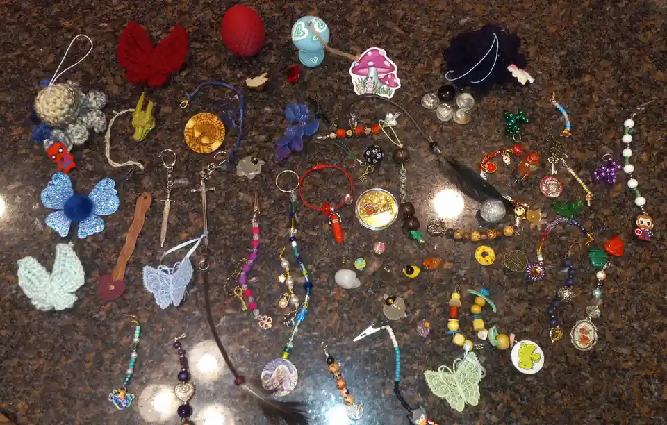 A top-down photo shows dozens of small, colorful, handmade or collectible items like charms, beads, keychains, and crocheted…