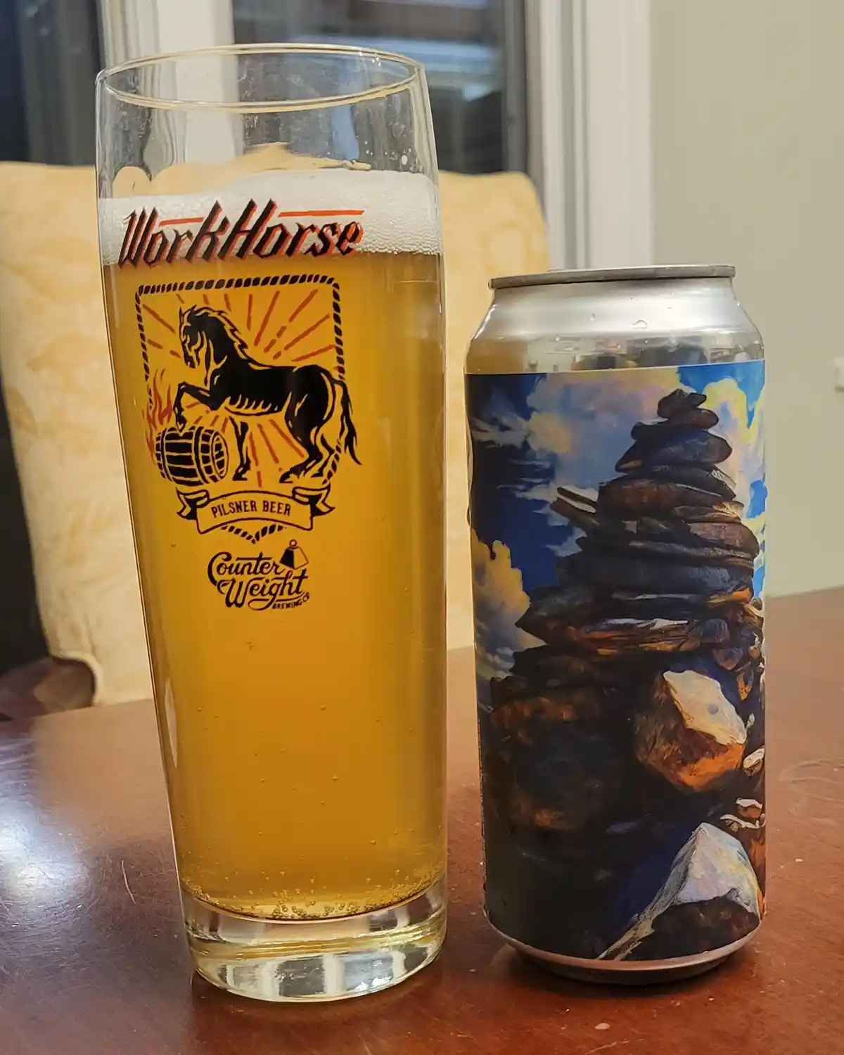 A tall glass filled with golden beer and a foamy head, branded with 'WorkHorse Pilsner Beer' and a horse logo, sits next to…