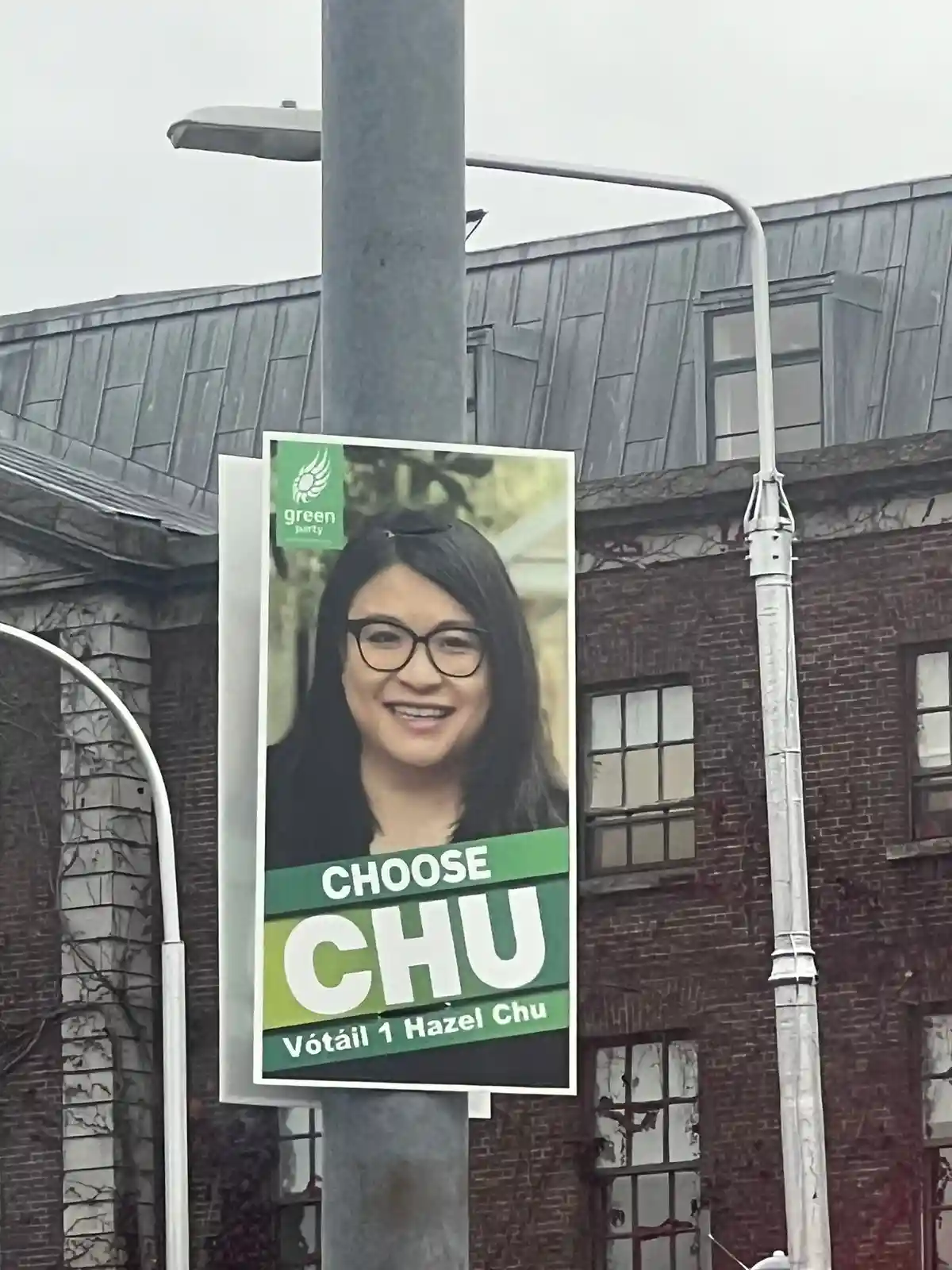 A political campaign poster for Hazel Chu, a candidate for the Green Party, is mounted on a street pole. The poster features…