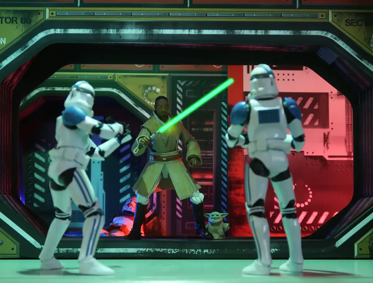 A Star Wars action figure scene shows a Jedi with a green lightsaber standing between two Stormtroopers in a futuristic…