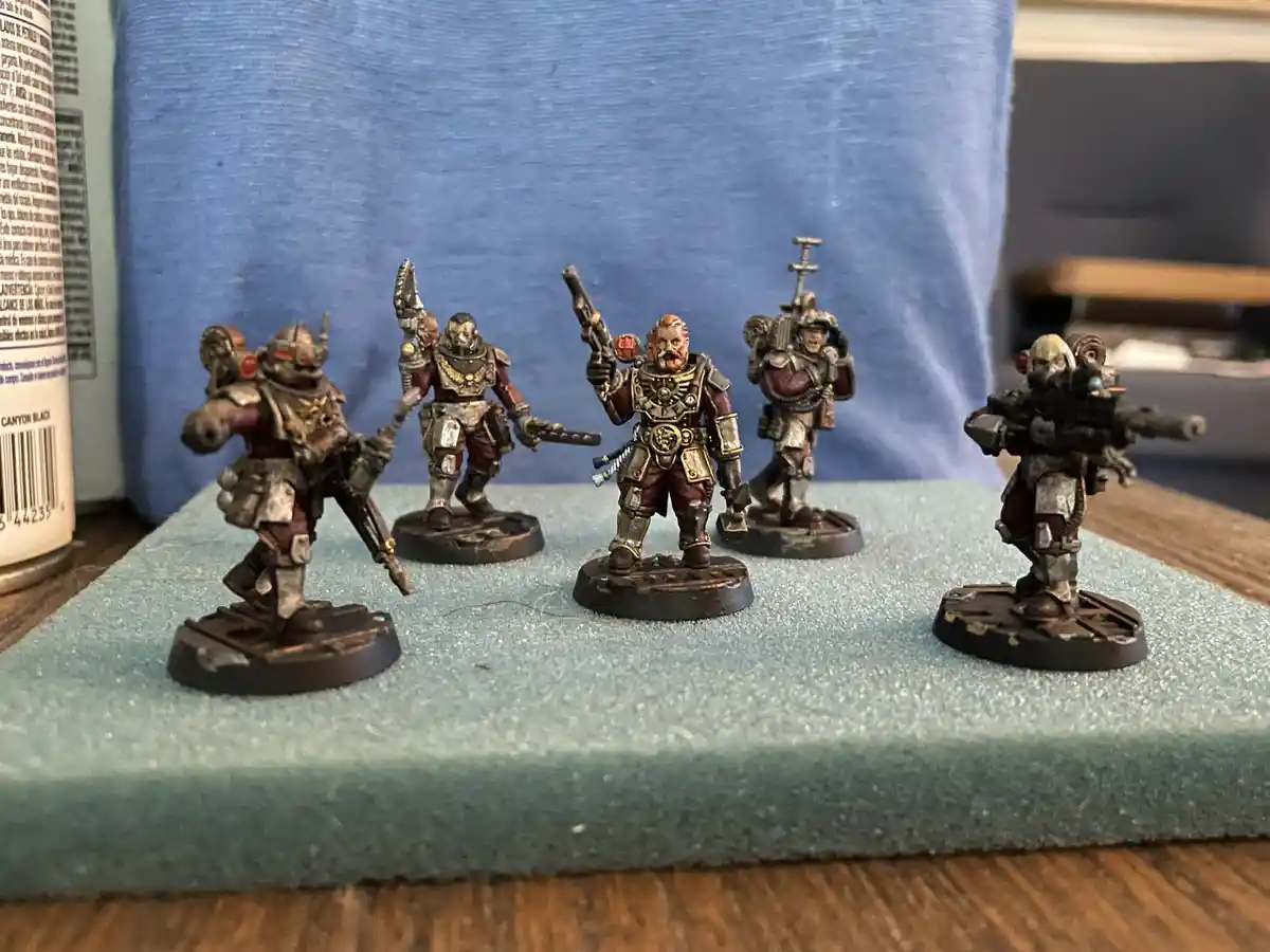 Five painted miniature figurines of armored warriors, likely from Warhammer 40,000, are arranged on a green foam mat. They…