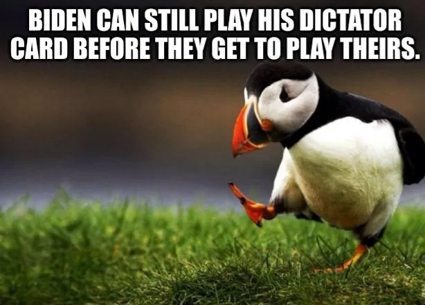 A close-up photo of a puffin standing on green grass, looking down and kicking one foot up slightly. The image has large…
