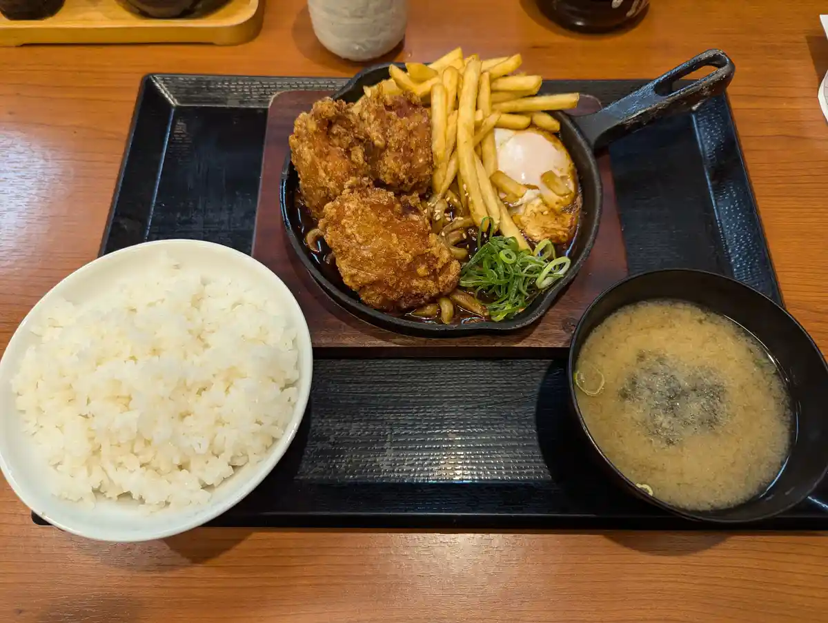 a japanese meal is presented on a wooden table, featuring a cast iron skillet with fried chicken, french fries, a…