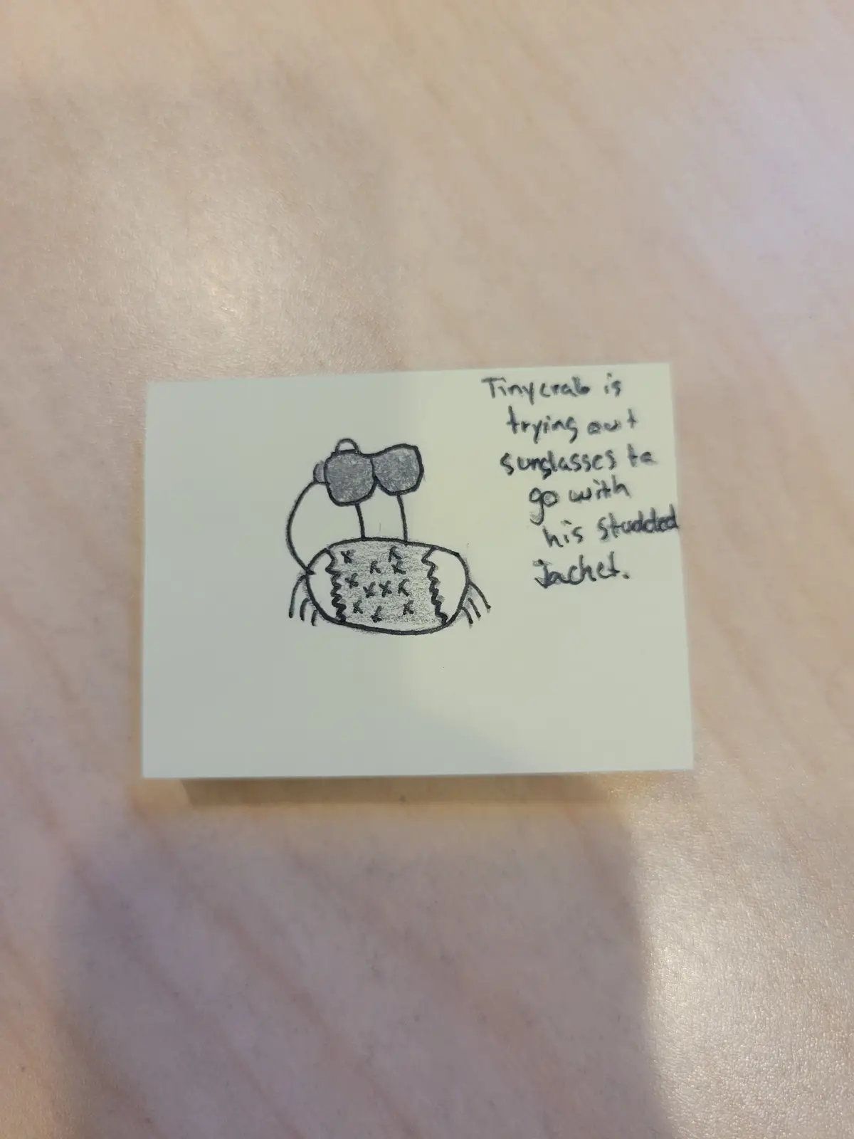 A hand-drawn sketch on a sticky note shows a cartoon crab wearing oversized sunglasses and a studded jacket. Beside the…
