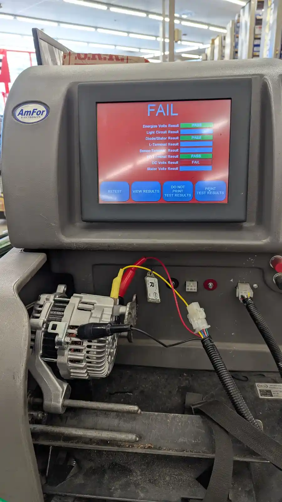 A close-up photo of an AmFor Electronics automotive alternator tester showing a red screen with the word 'FAIL' at the top…