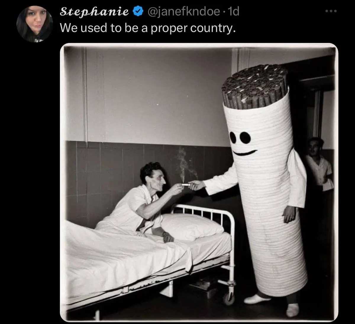 A black-and-white photo shows a man in a hospital bed smiling as a person in a large, smiling cigarette costume hands him a…