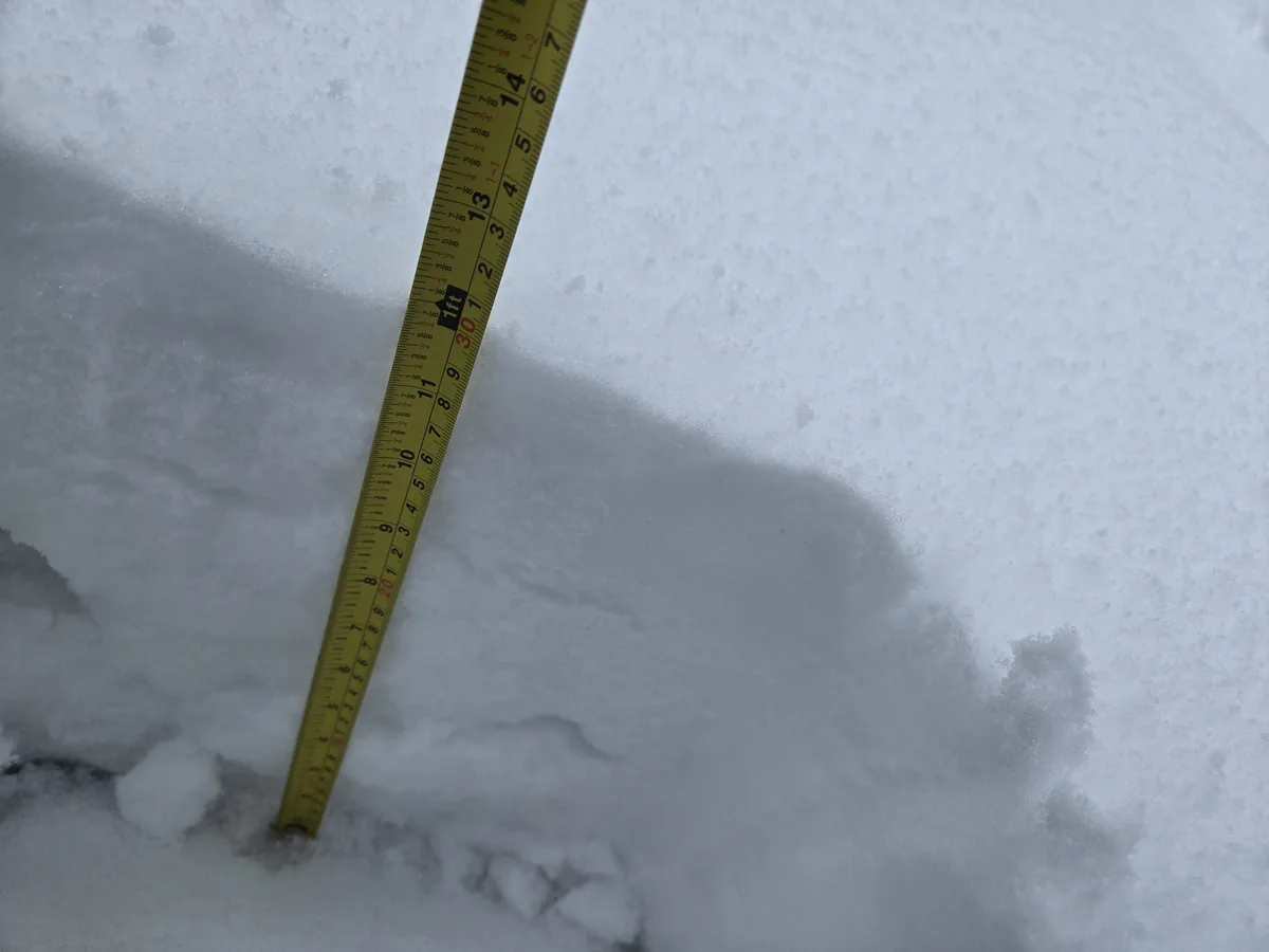 A yellow measuring tape is stuck vertically into a deep layer of snow, showing the measurement '30' inches. The snow is…