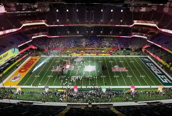 a wide-angle view of an empty indoor football stadium with the field marked for a game between the chiefs and the eagles…