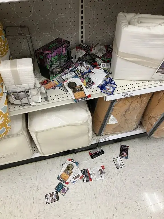 A retail store shelf, likely in a home goods section, is cluttered with scattered trading cards and booster packs spilling…