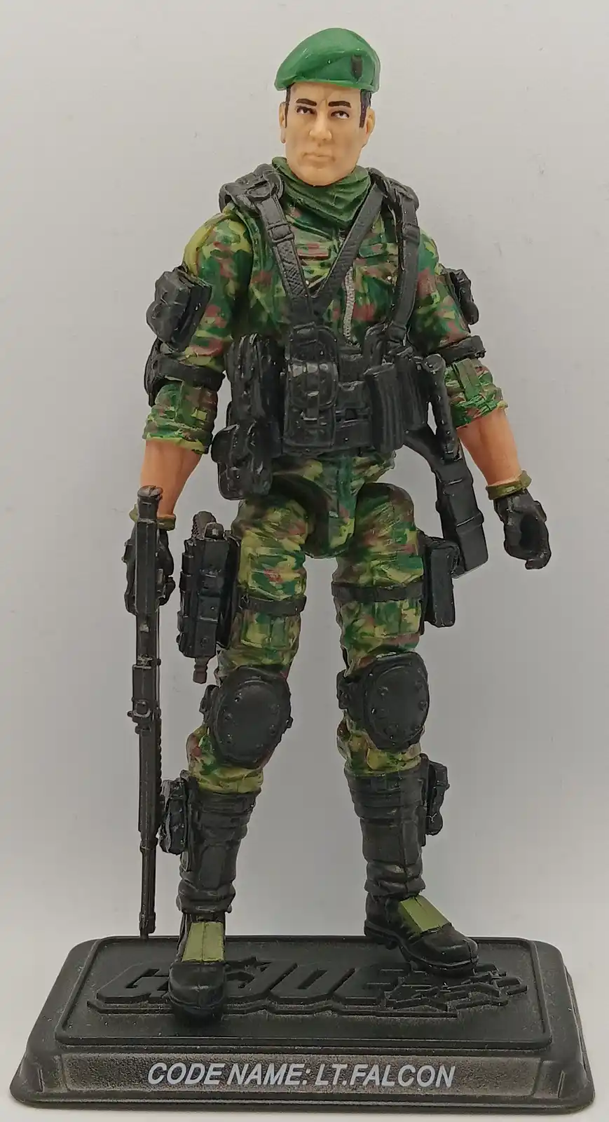 A G.I. Joe action figure in full camouflage gear with a green beret, holding a rifle and wearing tactical vest and knee…