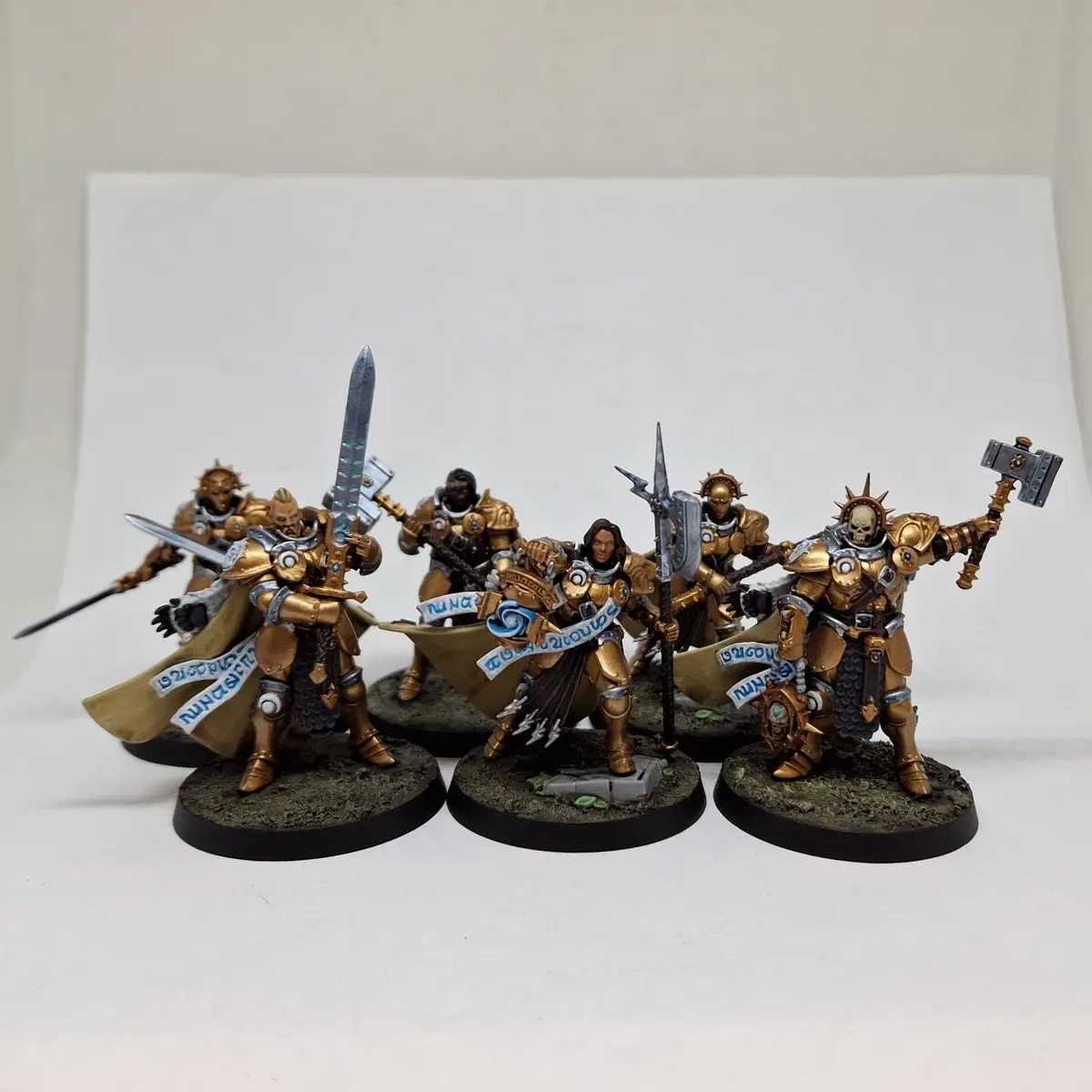 Five intricately painted miniature fantasy warriors in golden armor stand on circular bases against a plain white…
