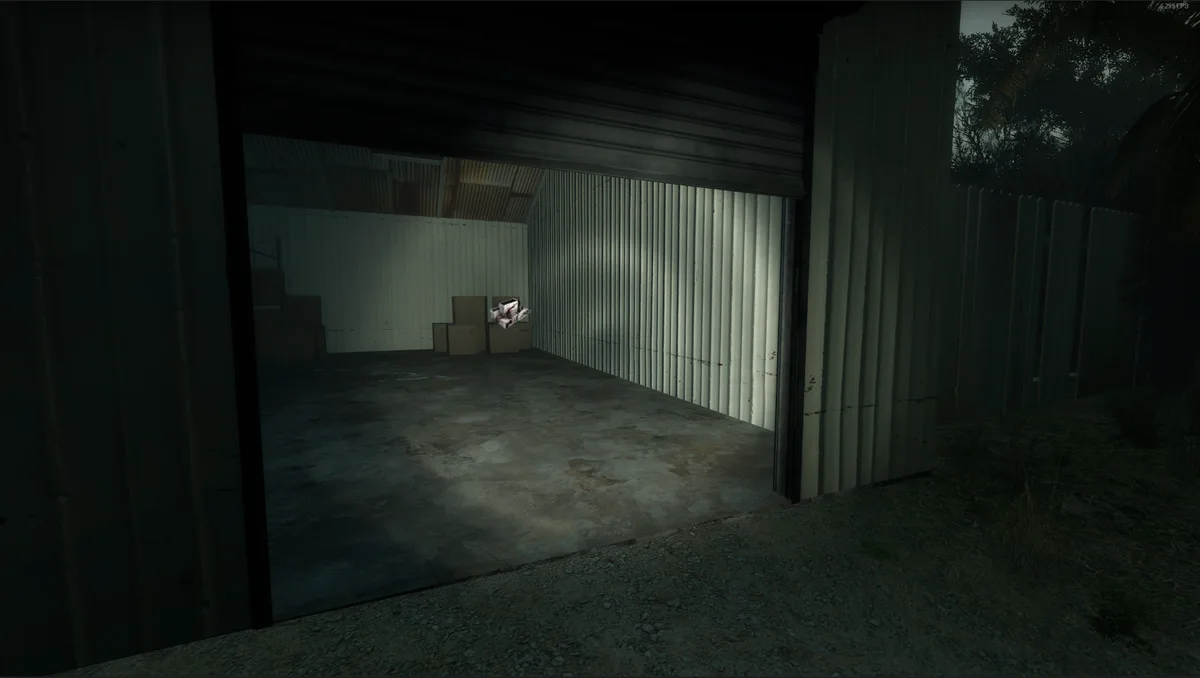 A dimly lit, empty storage unit with corrugated metal walls and a partially open roll-up door. Inside, a few cardboard boxes…