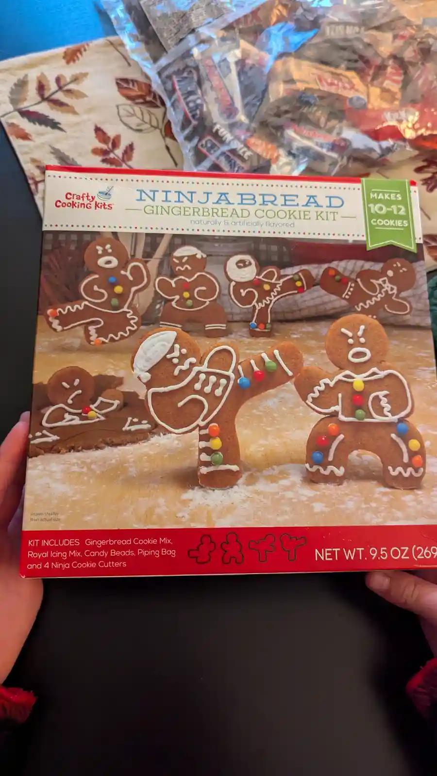 A person holds a 'NINJABREAD GINGERBREAD COOKIE KIT' box featuring cartoon gingerbread men in ninja poses with white icing…