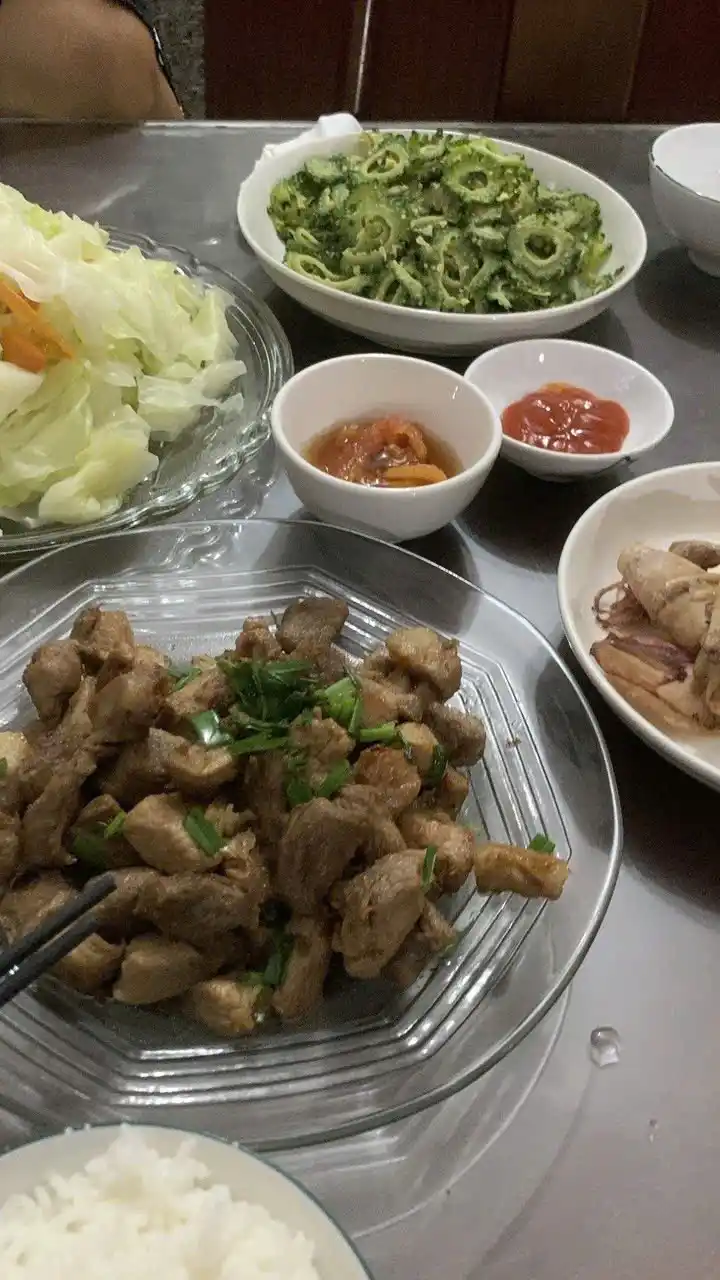 A table full of Asian-style dishes including stir-fried meat with green onions, bitter melon, cabbage salad, rice, and…