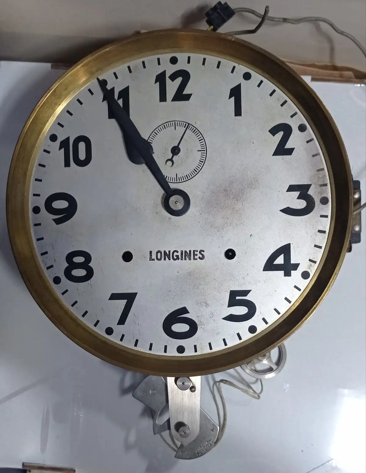 A close-up of a vintage Longines wall clock with a brass rim and white face, showing the time as approximately 10:55. The…