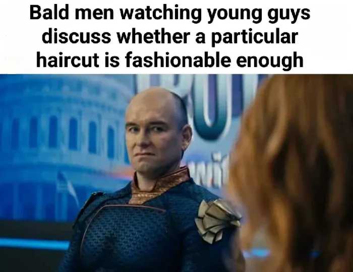 A bald man in a blue patterned costume with gold shoulder accents stares intently at a woman with long brown hair, whose…