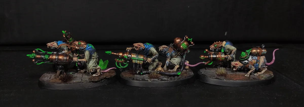 Three painted miniature rat-like warband figures, each wielding a large, steampunk-style green energy weapon, are arranged…