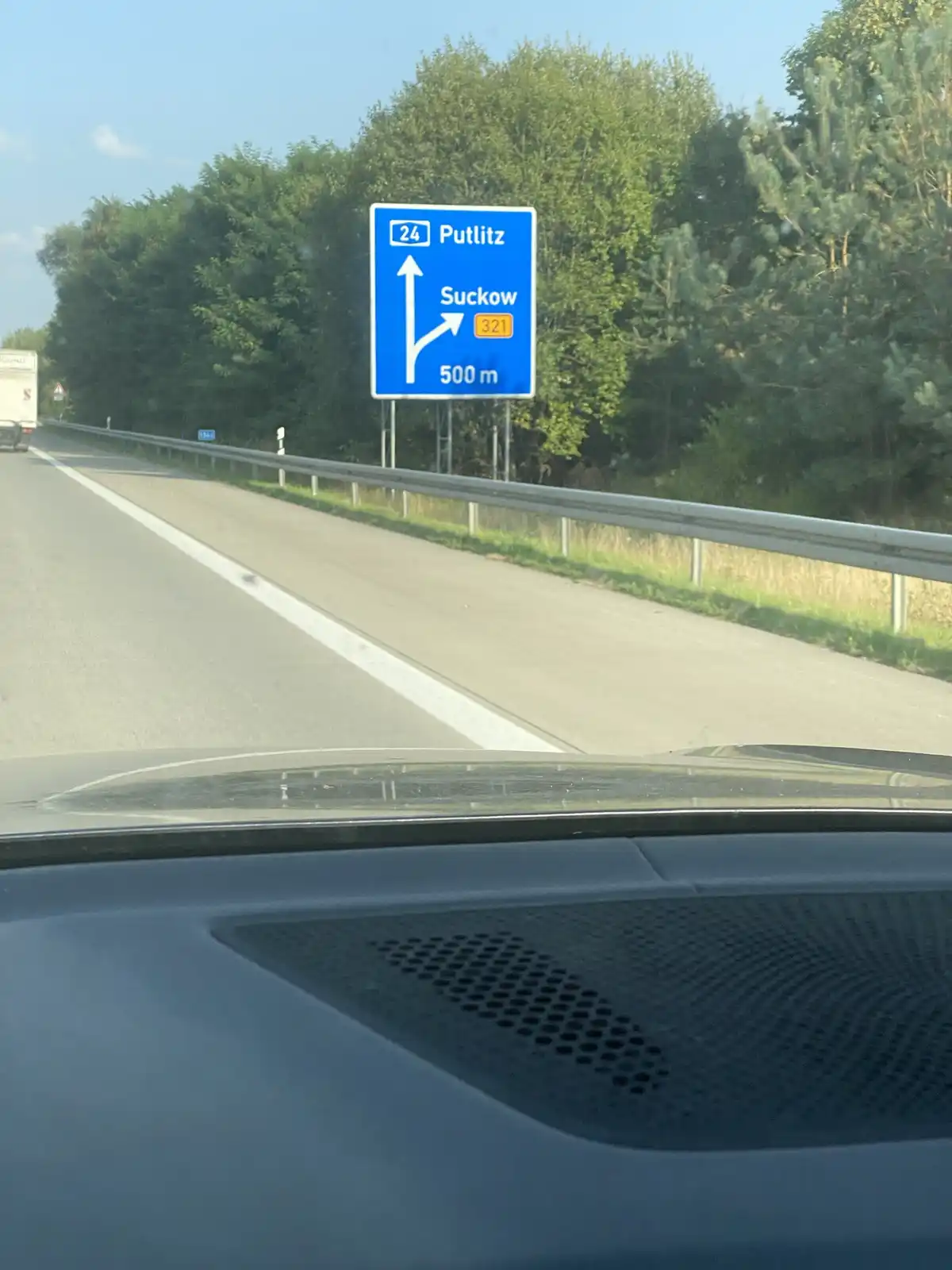 A photo taken from inside a car shows a blue German highway sign indicating 'Putlitz' straight ahead and 'Suckow 321' to the…