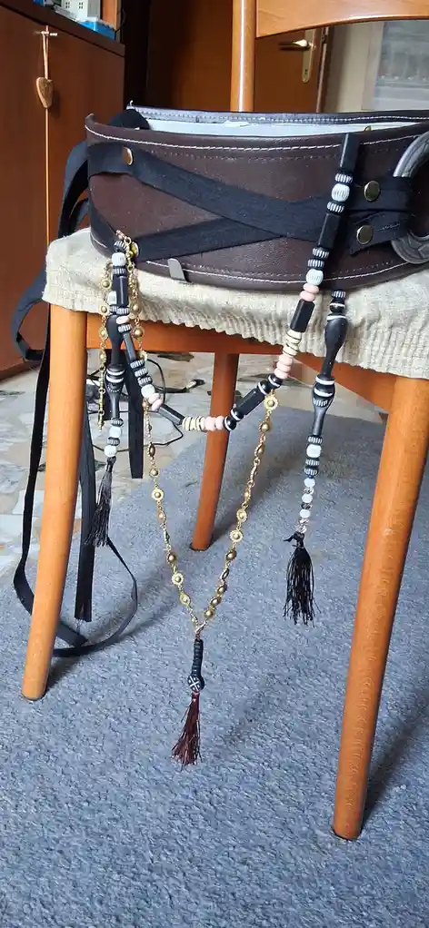 A brown leather belt with black straps and multiple decorative chains, beads, and tassels hangs over the back of a wooden…