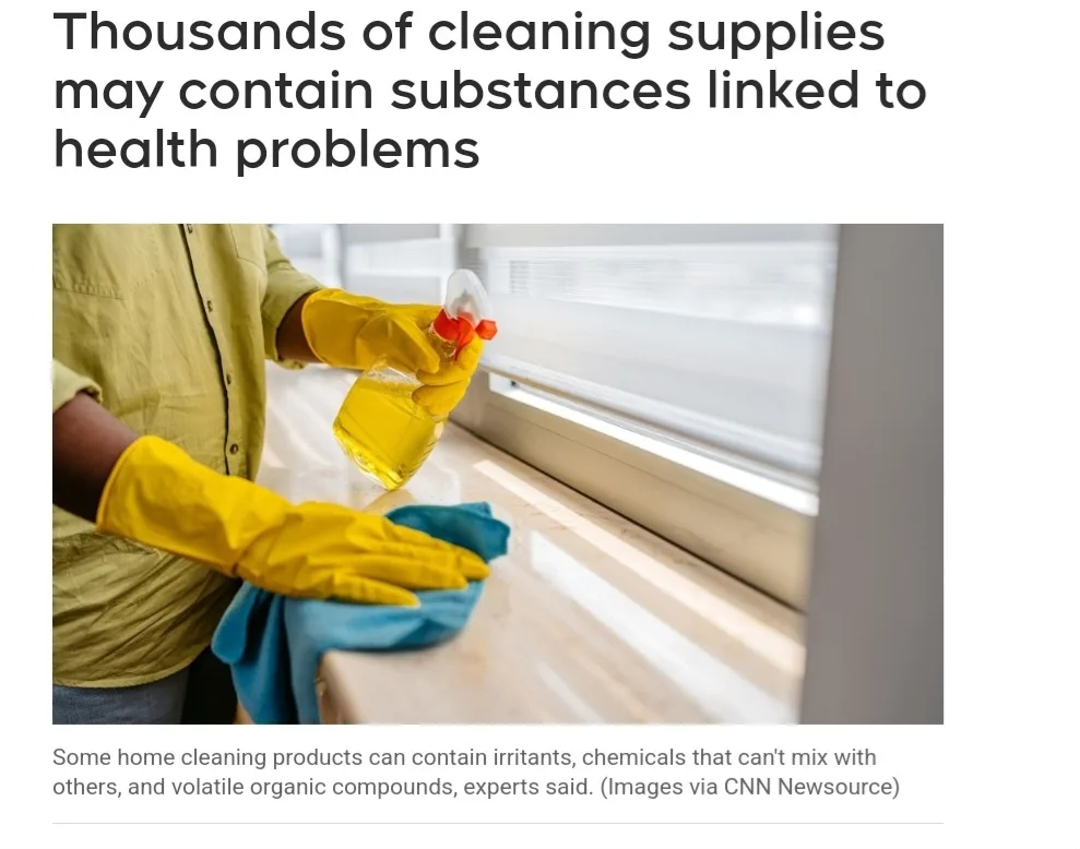 A person wearing yellow rubber gloves sprays a cleaning solution from a bottle onto a windowsill while wiping it with a blue…