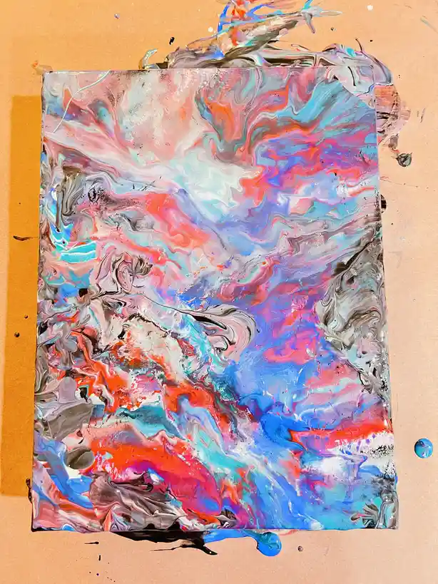 A rectangular canvas with vibrant, swirling abstract paint in shades of blue, pink, red, white, and gray, resting on a brown…