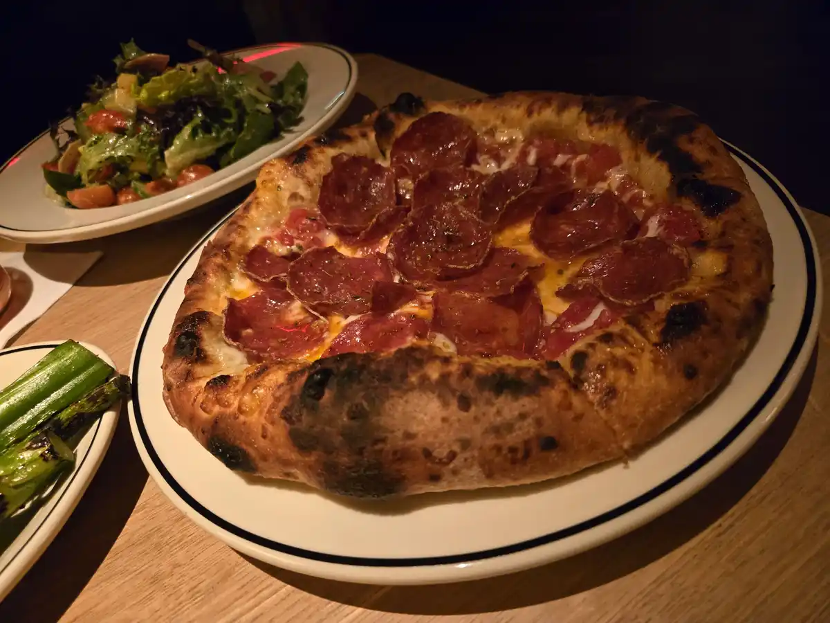 A close-up photo of a thick-crust pizza with pepperoni and tomato sauce, served on a white plate with a black rim, alongside…