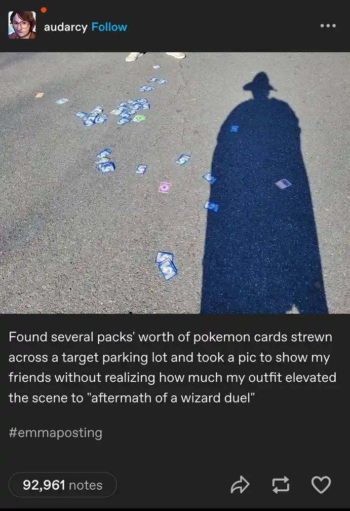 A photo shows numerous Pokémon trading cards scattered across an asphalt parking lot, with a long, dark shadow of a person…