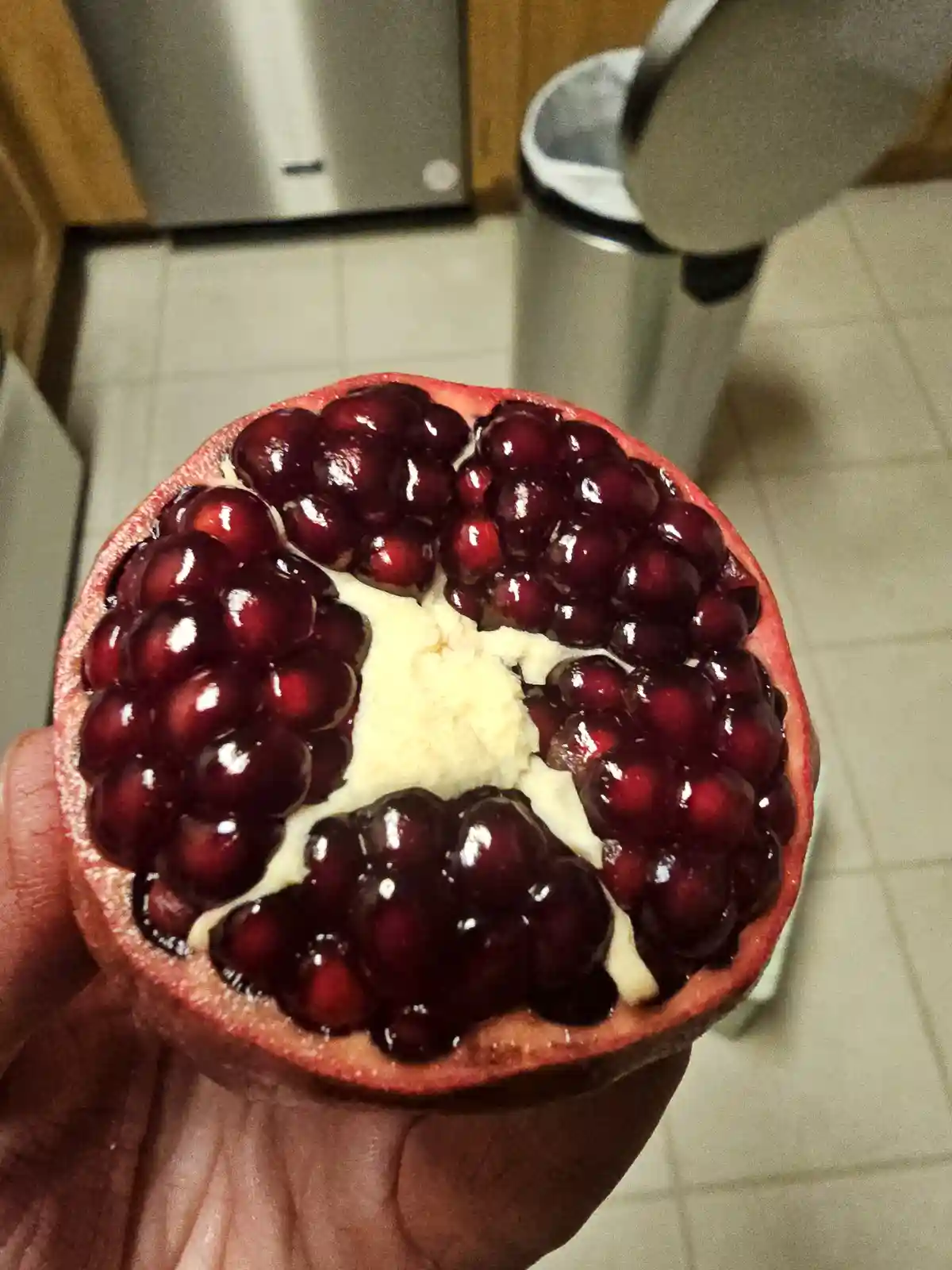 A hand holds a halved pomegranate, revealing its juicy red arils arranged in a circular pattern around a pale, fibrous…