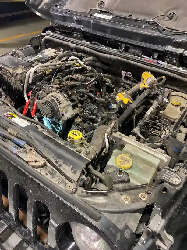 A close-up photo of a car's engine bay with the hood open, showing a cluttered and dirty engine with various tools like a…