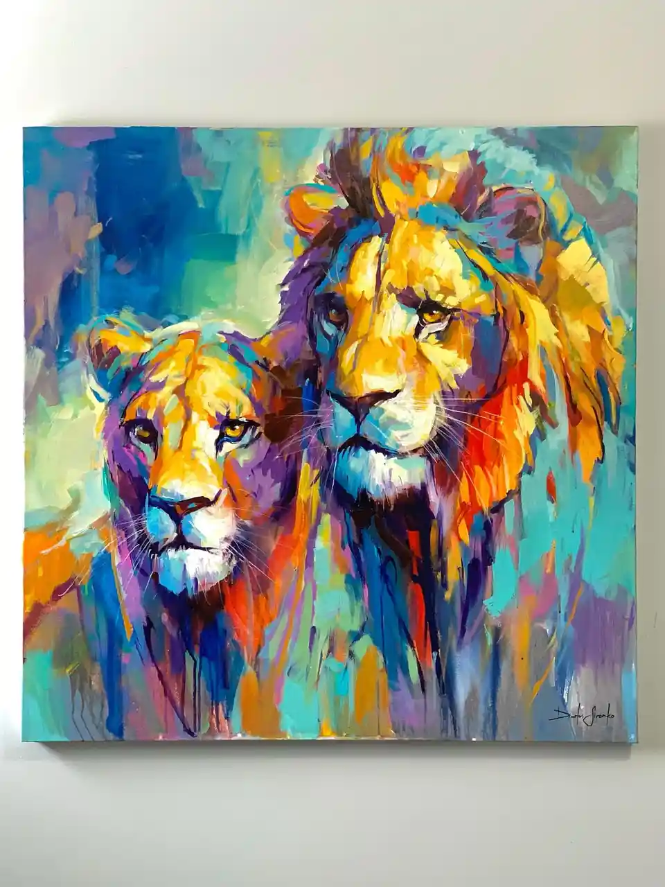 A colorful abstract painting of two lions, one larger male with a mane and one smaller female, both facing forward. The…